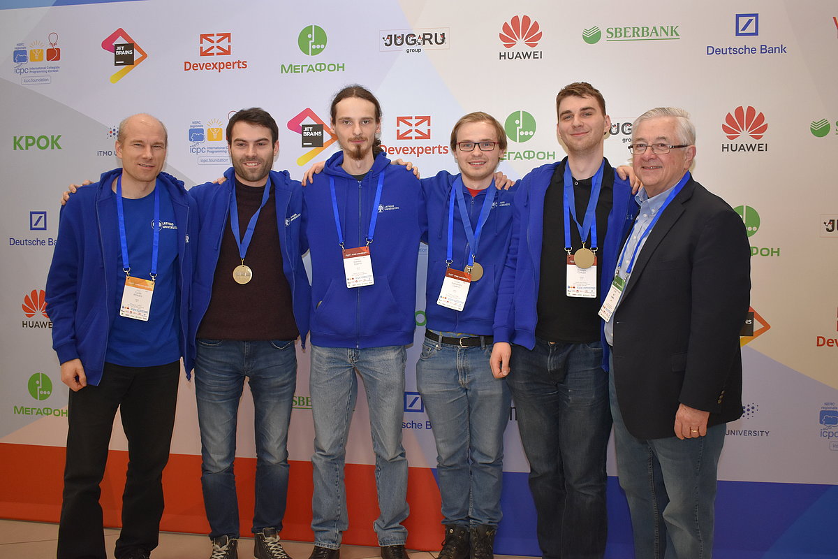 LU komanda kopā ar treneriem un ICPC direktoru Bilu Paučeru 2019. gada pusfinālā, iegūstot bronzas medaļu un ceļazīmi uz finālu. No kreisās: komandas treneris Guntis Arnicāns, komandas treneris Jevgēnijs Vihrovs, Aleksejs Zajakins, Aleksandrs Zajakins, Kristaps Čivkulis, ICPC direktors Bils Paučers.