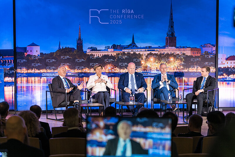 Foto no Rīgas konferences 2025, redzama skatuve un paneļa dalībnieki