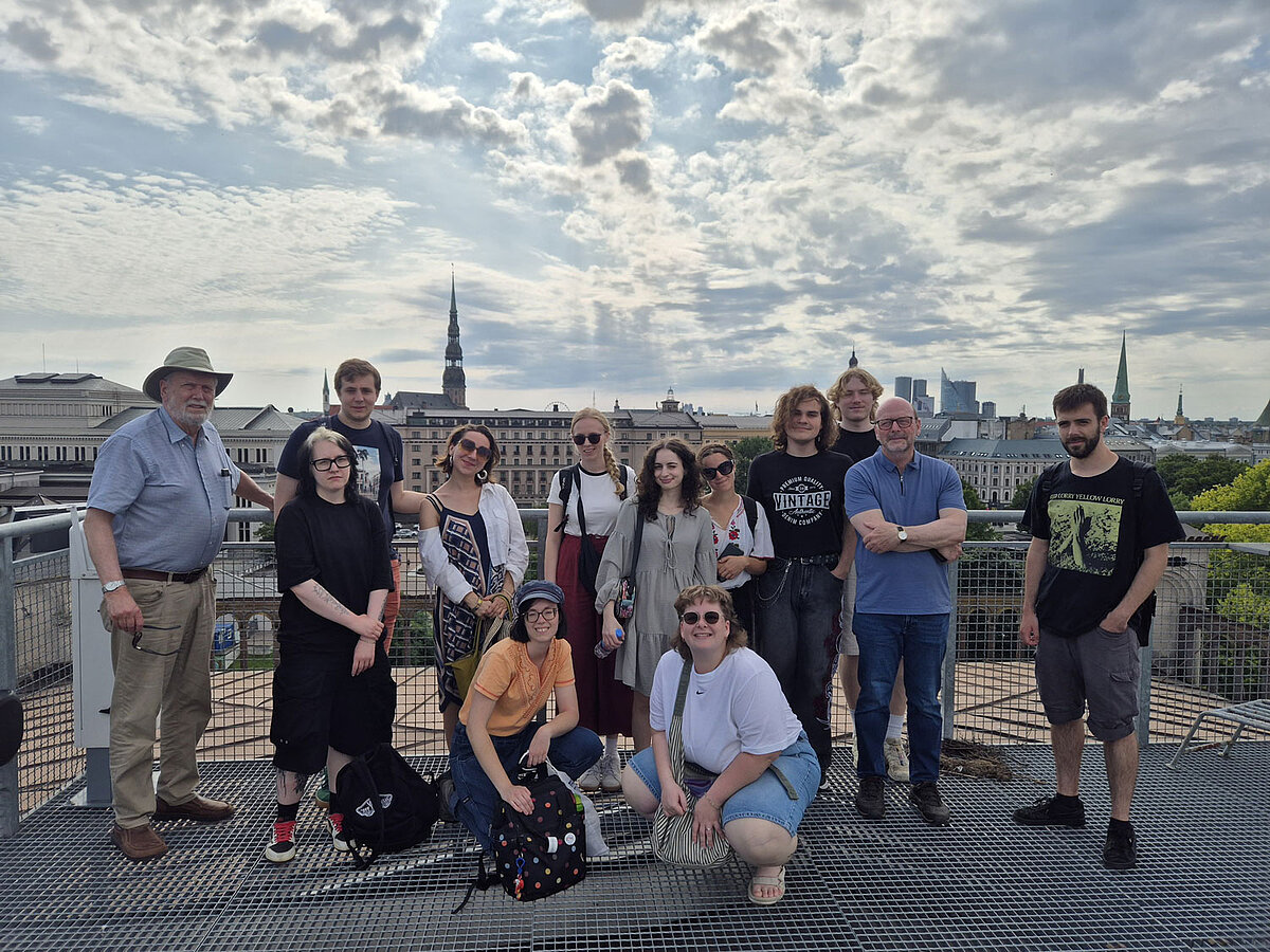 Latviešu valodas un kultūras vasaras skolas dalībnieki uz terases ar skatu uz Rīgas panorāmu.