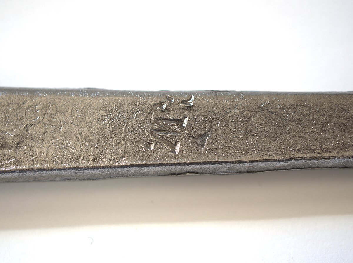 11. att. Notīrīts korozijas slānis un abreviatūra C.W. uz rapiera asmens astes daļas. Foto: Gints Ajausks 11. att. Notīrīts korozijas slānis un abreviatūra C.W. uz rapiera asmens astes daļas. Foto: Gints Ajausks