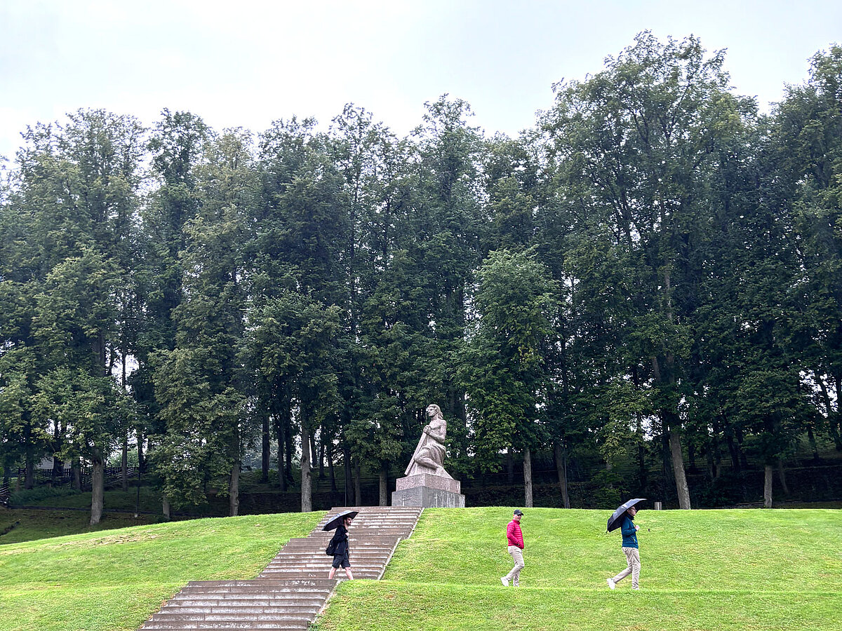 Vasaras skolas dalībnieki pie pieminekļa parkā lietainā laikā.
