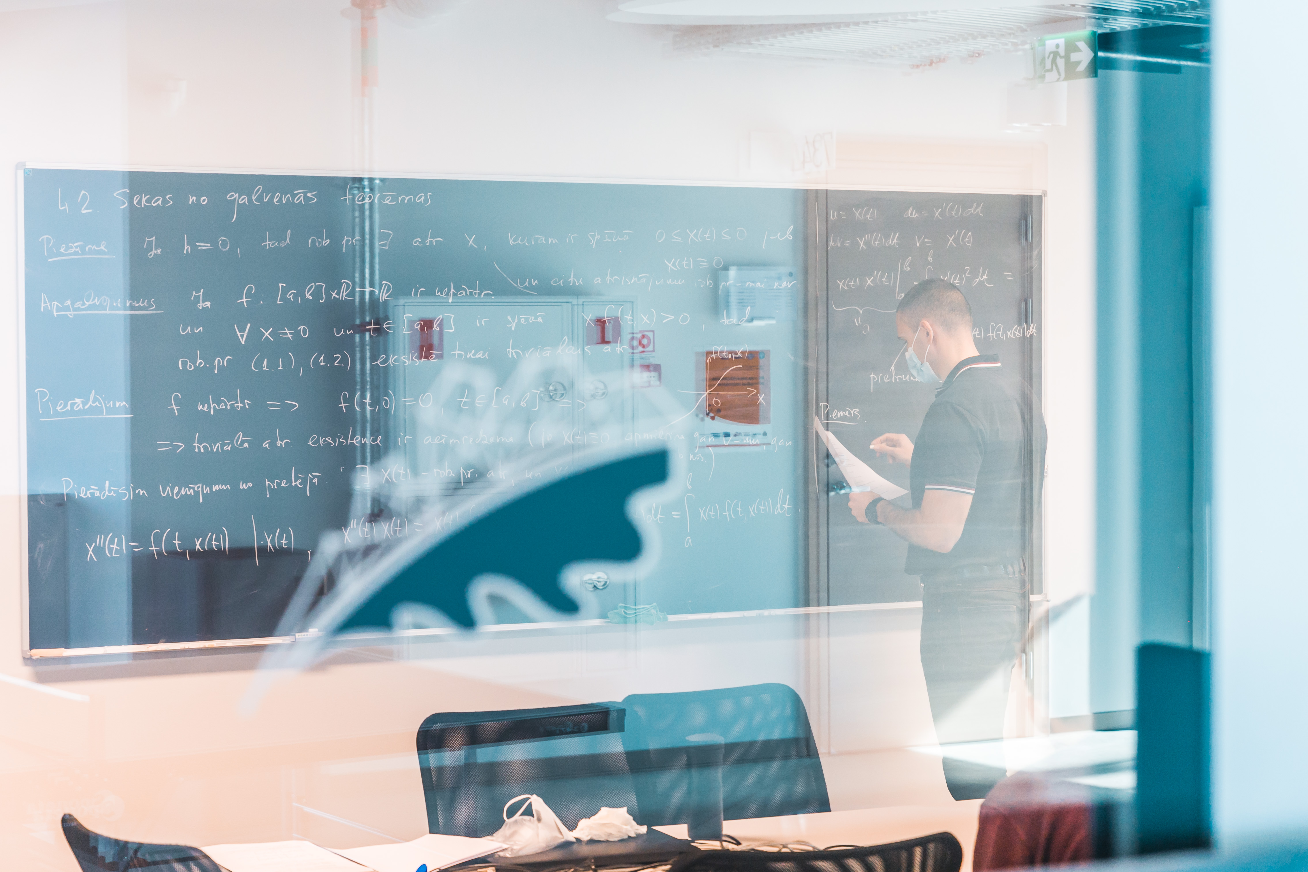 Students pie tāfeles, uz kuras rakstītas dažādas formulas