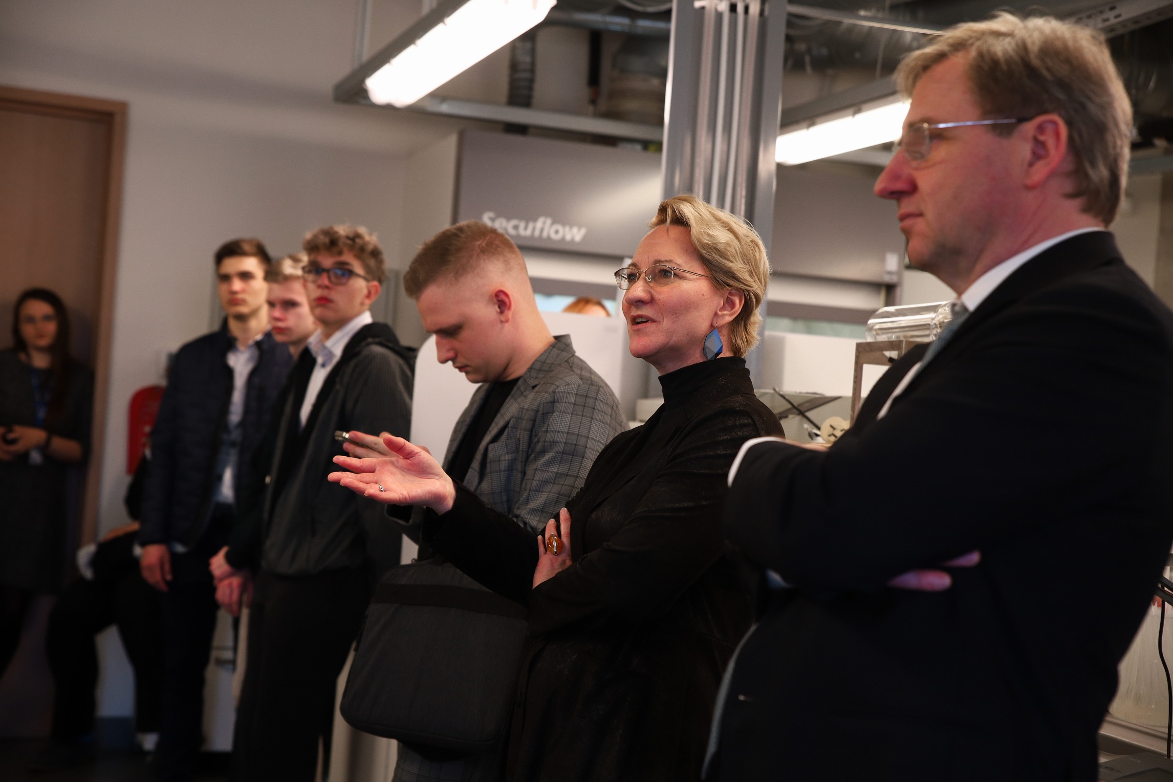 Cilvēku grupa klausās stāstījumu, atrodoties laboratorijā