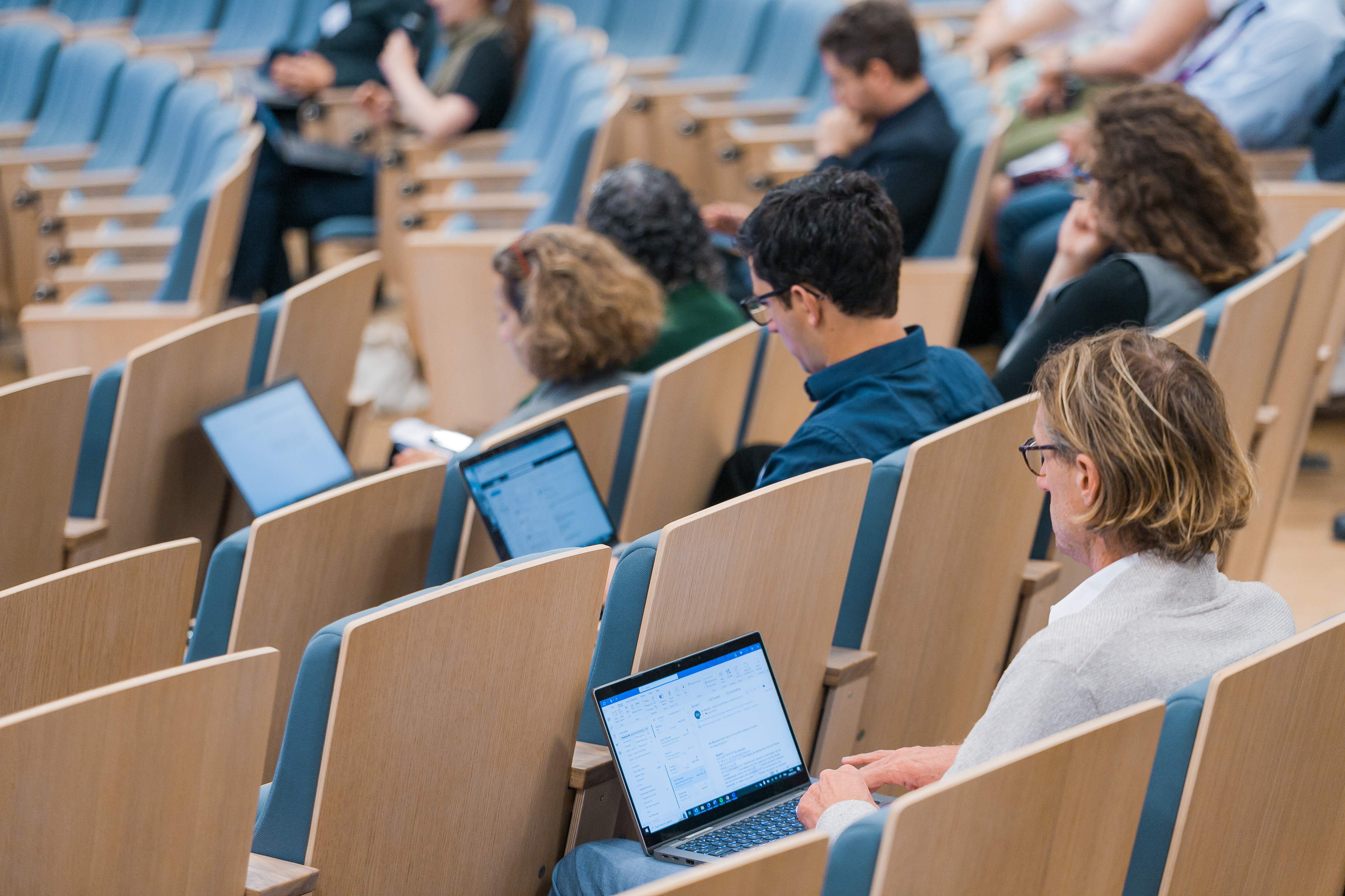 Studenti sēž ar muguru auditorijā ar atvērtiem klēpjdatoriem