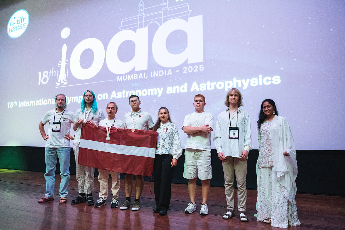 Latvijas skolēnu komanda ar valsts karogu un izcīnītajām medaļām 18. Starptautiskajā astronomijas un astrofizikas olimpiādē Mumbajā, Indijā 2025. gadā.