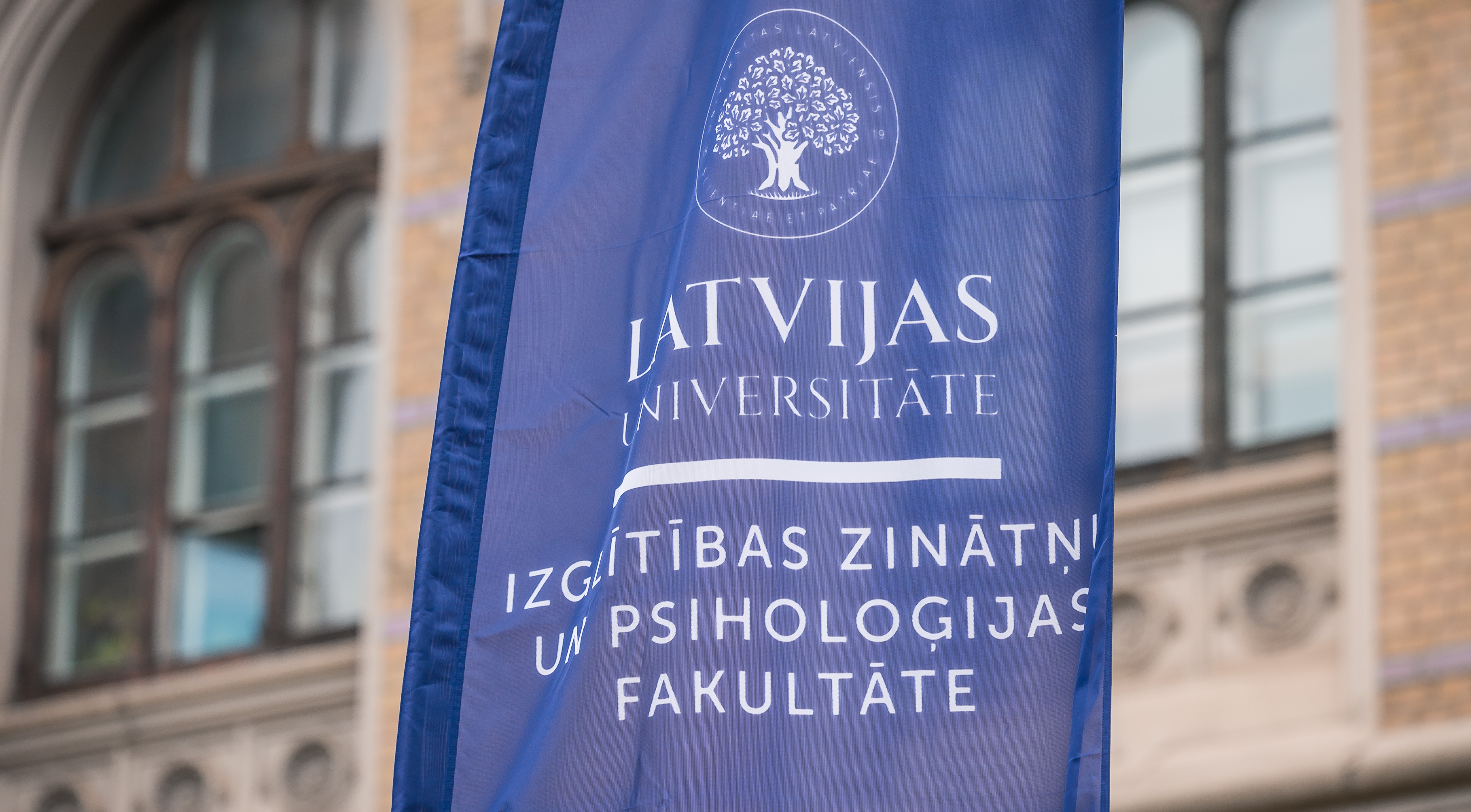 Karogs ar uzrakstu "Latvijas Universitāte. Izglītības zinātņu un psiholoģijas fakultāte". Fonā LU galvenā ēka. 