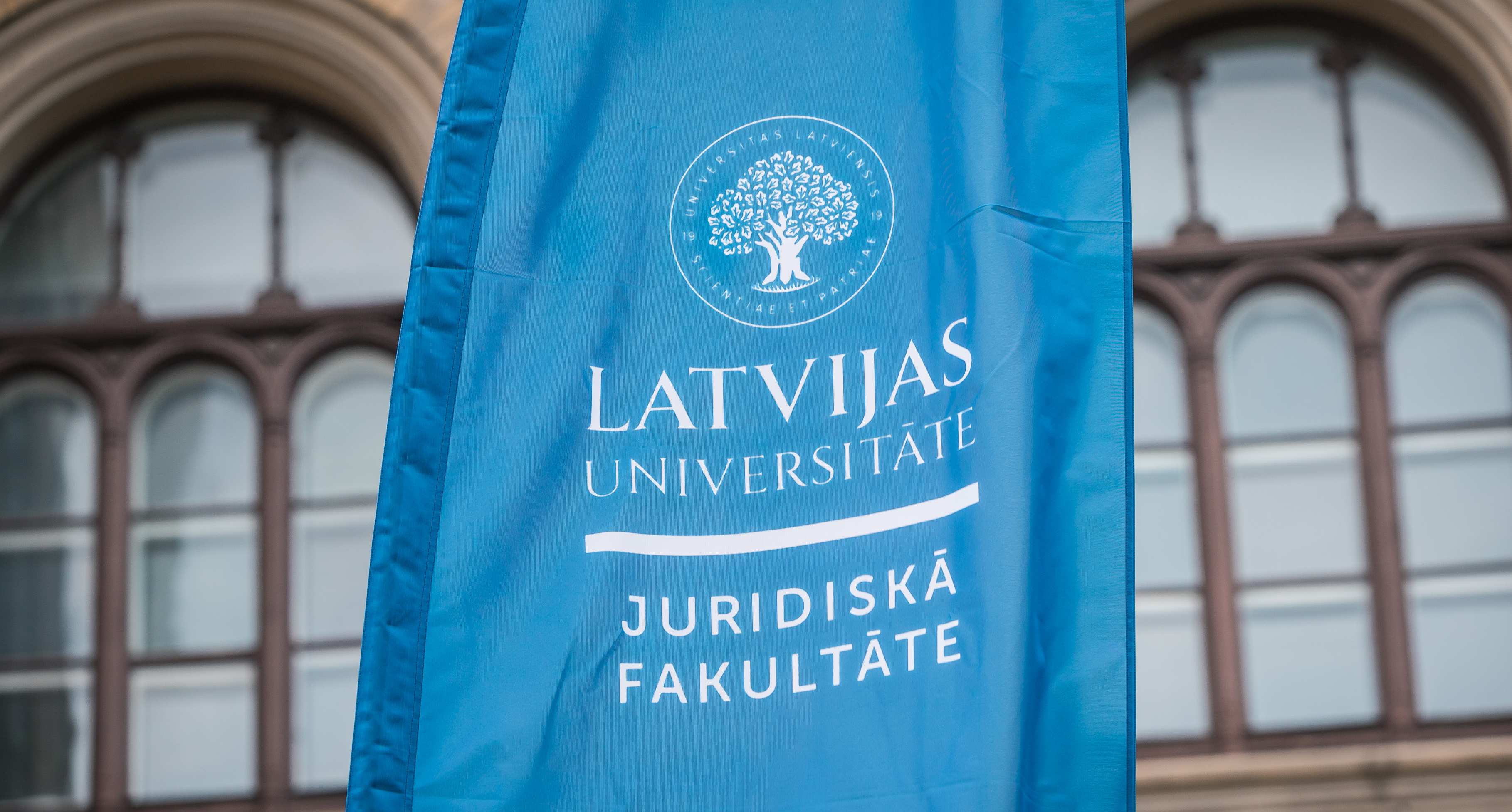 LU ēka un zils karogs ar uzrakstu "Latvijas Universitāte. Juridiskā fakultāte"