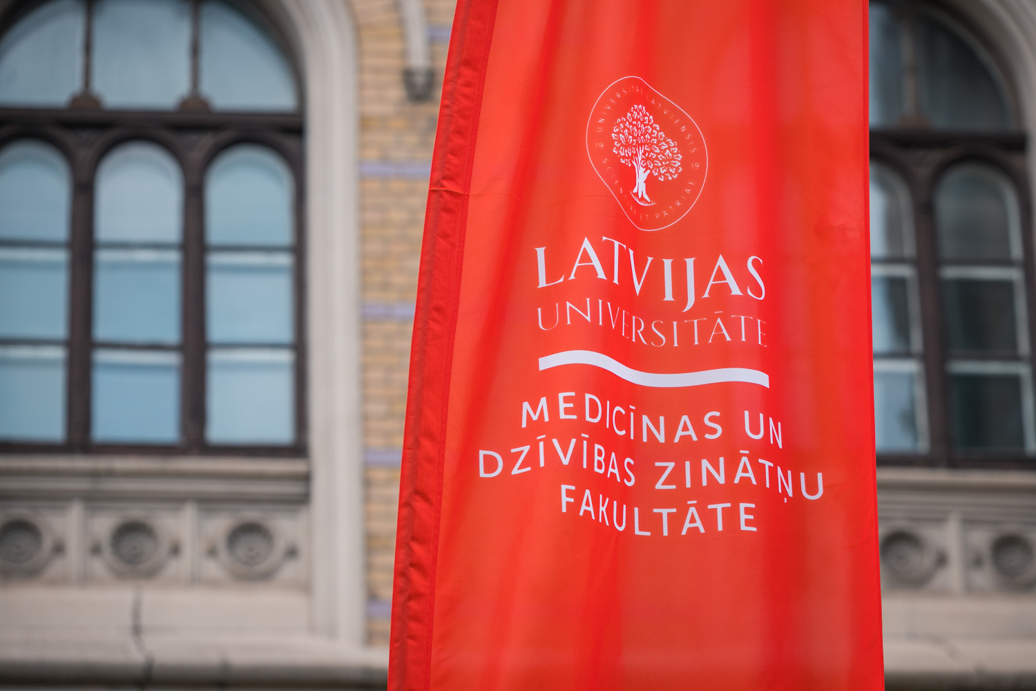 Medicīnas un dzīvības zinātņu fakultātes karogs uz LU galvenās ēkas fona