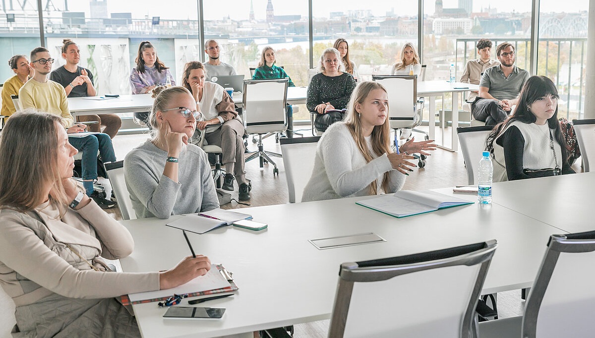 Cilvēki sēž pie galdiem auditorijā
