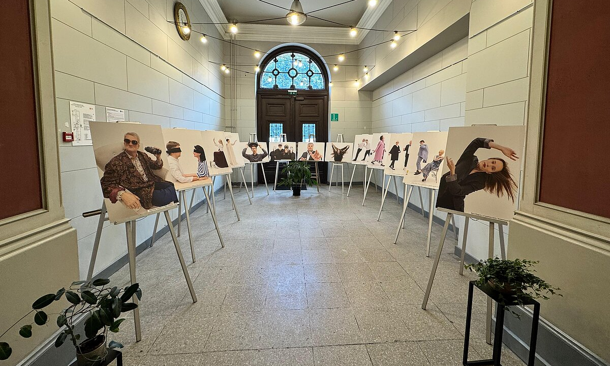 Gaitenis ar molbertiem, uz kuriem izstādītas cilvēku fotogrāfijas