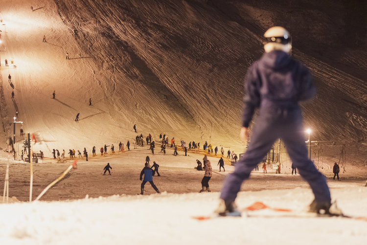 Cilvēks uz slēpēm un fonā kalns, citi slēpotāji un sniegs