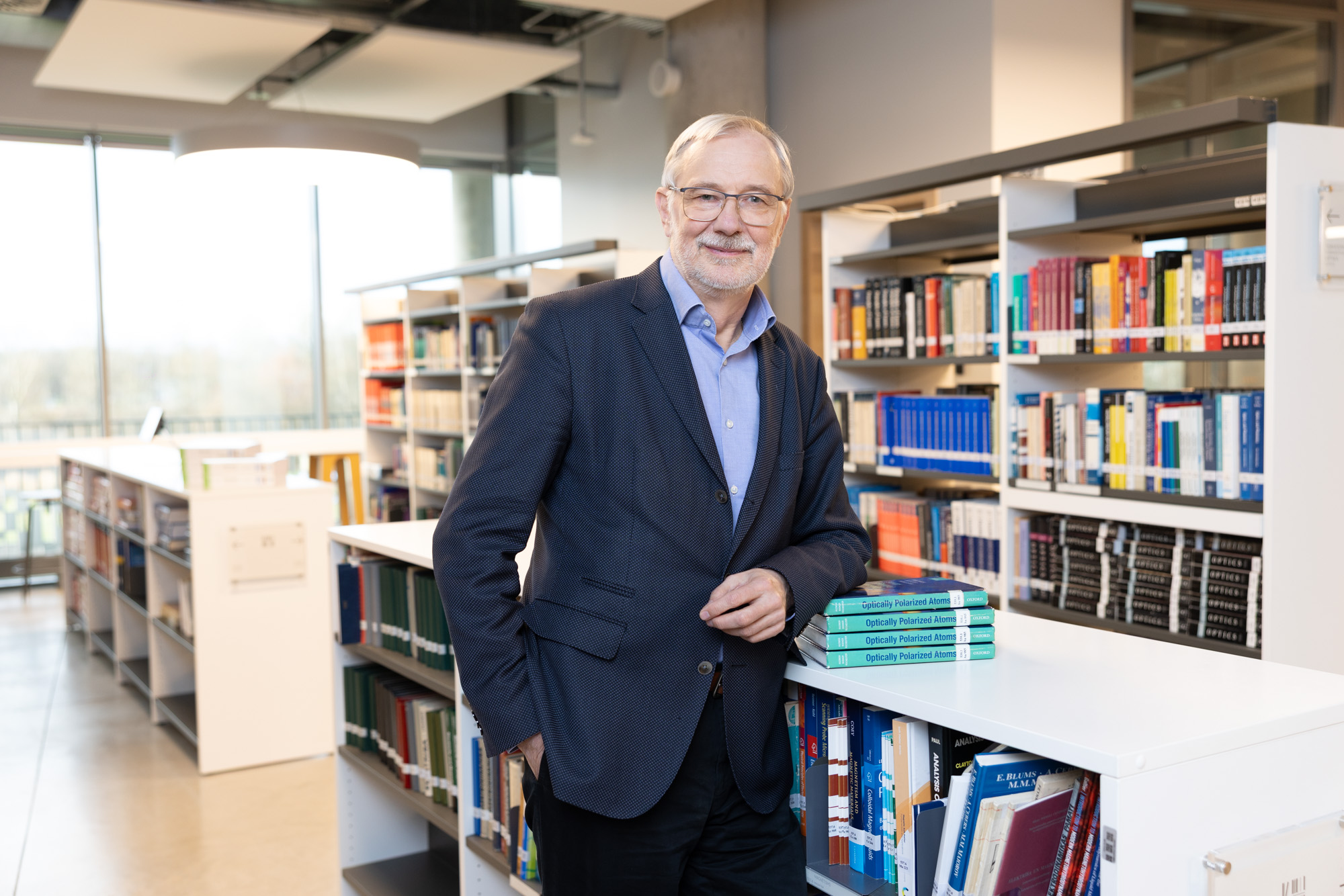 LU profesors Mārcis Auziņš pie grāmatu plaukta. Fonā bibliotēka ar grāmatām plauktos. 