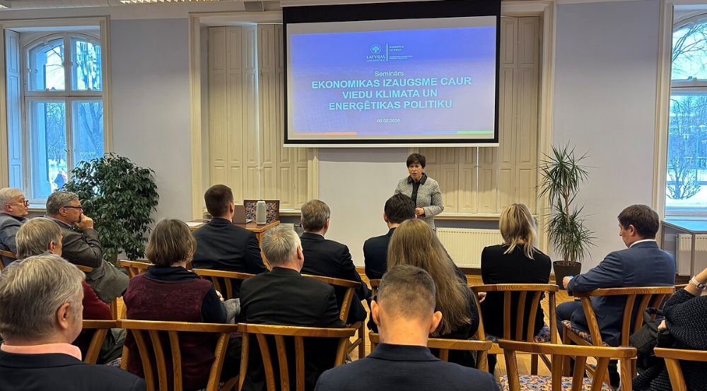 Semināra telpa ar klausītājiem, kuri sēž rindās un vēro priekšā notiekošu prezentāciju. Uz ekrāna redzams semināra nosaukums “Ekonomikas izaugsme caur viedu klimata un enerģētikas politiku”. Pie ekrāna stāv runātājs, bet telpā aiz logiem redzams ziemīgs skats.