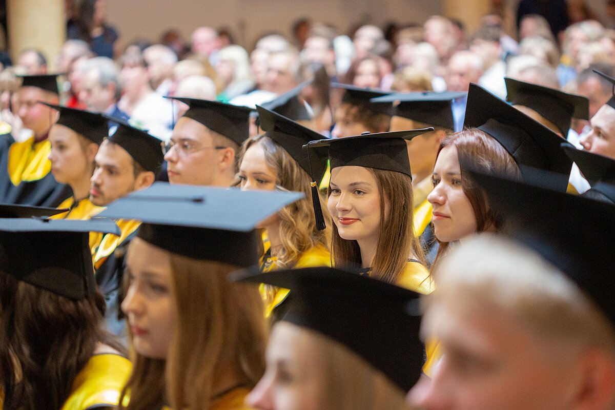 Izlaiduma ceremonijas dalībnieki auditorijā, tērpti absolventu tērpos 
