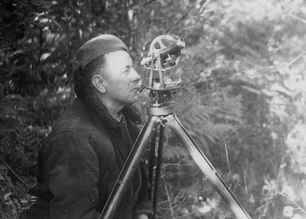 Persona mežainā vidē strādā ar uz statīva uzstādītu ģeodēzisko instrumentu